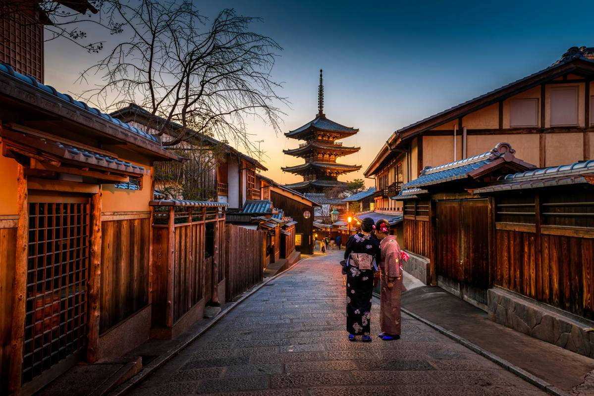 Two women in kimono walking through Gion district Kyoto at sunset with pagoda in background