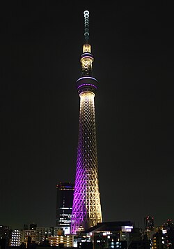 Tokyo Skytree tower illuminated in purple and gold at night against dark sky